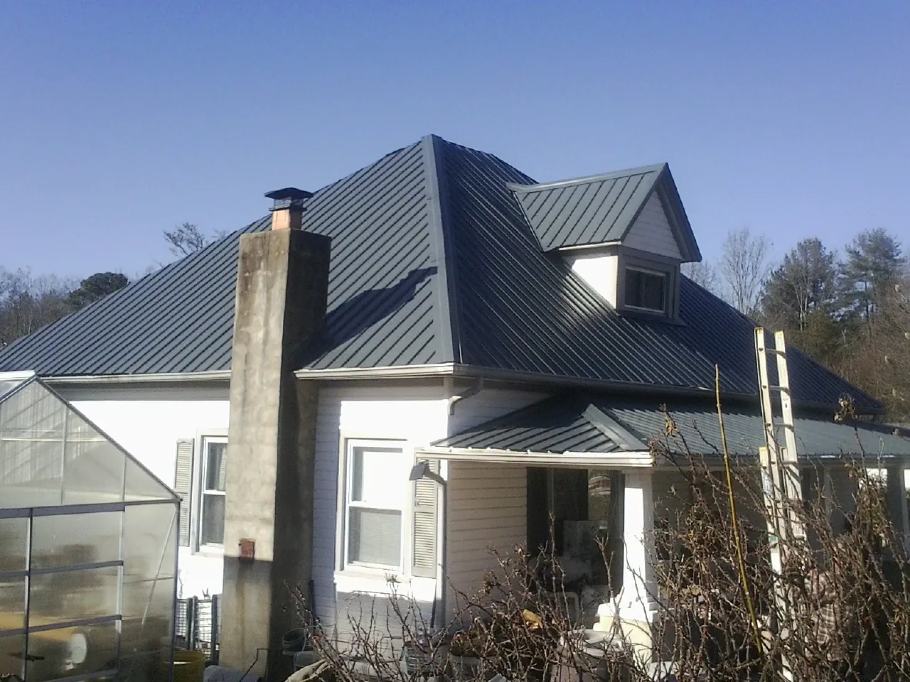 Dark blue standing seam metal roof on a white farmhouse with dormer — Slate & Tile Roof Repair by Roofing Brothers in Beecher