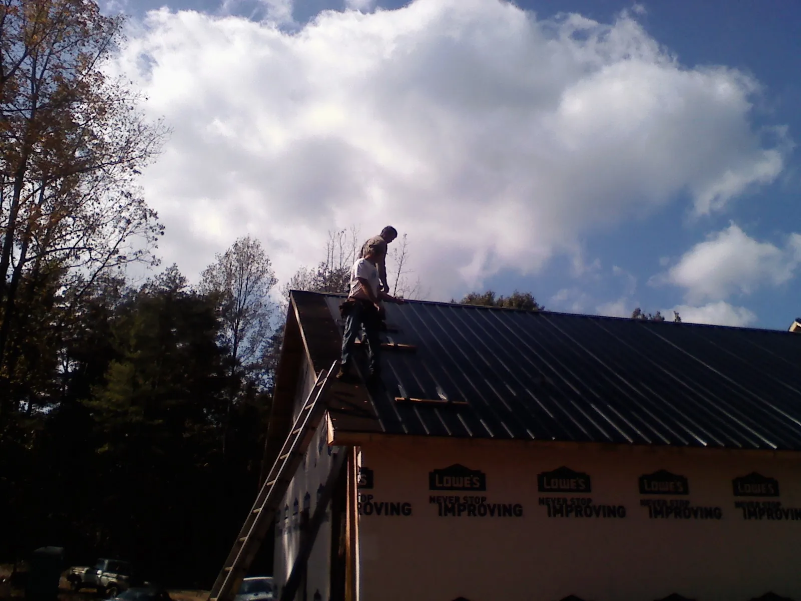 Roofer fastening dark metal panels high against a cloudy sky, from a Roof Inspection job in Beecher