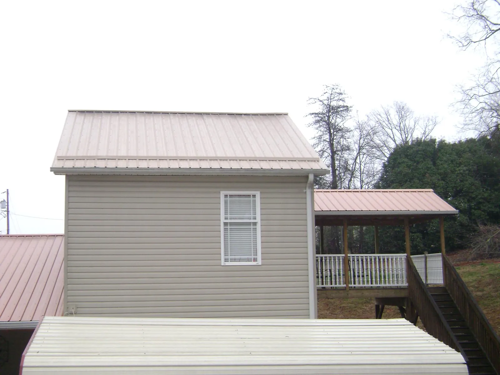 Tan metal roofs on a two story addition and attached porch, from a Roof Replacement job in Beecher